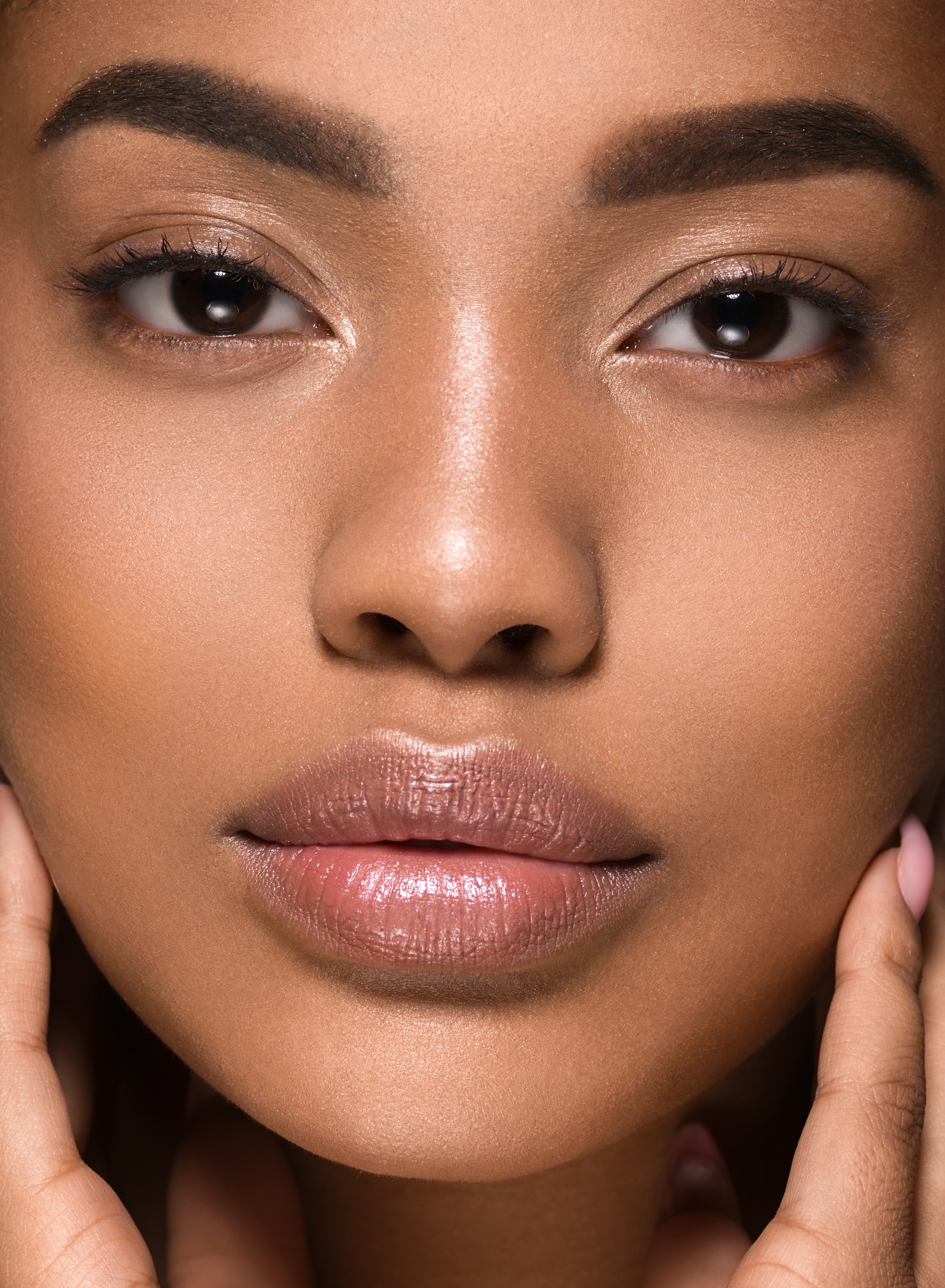 Melanated woman with glowing skin cradling her face